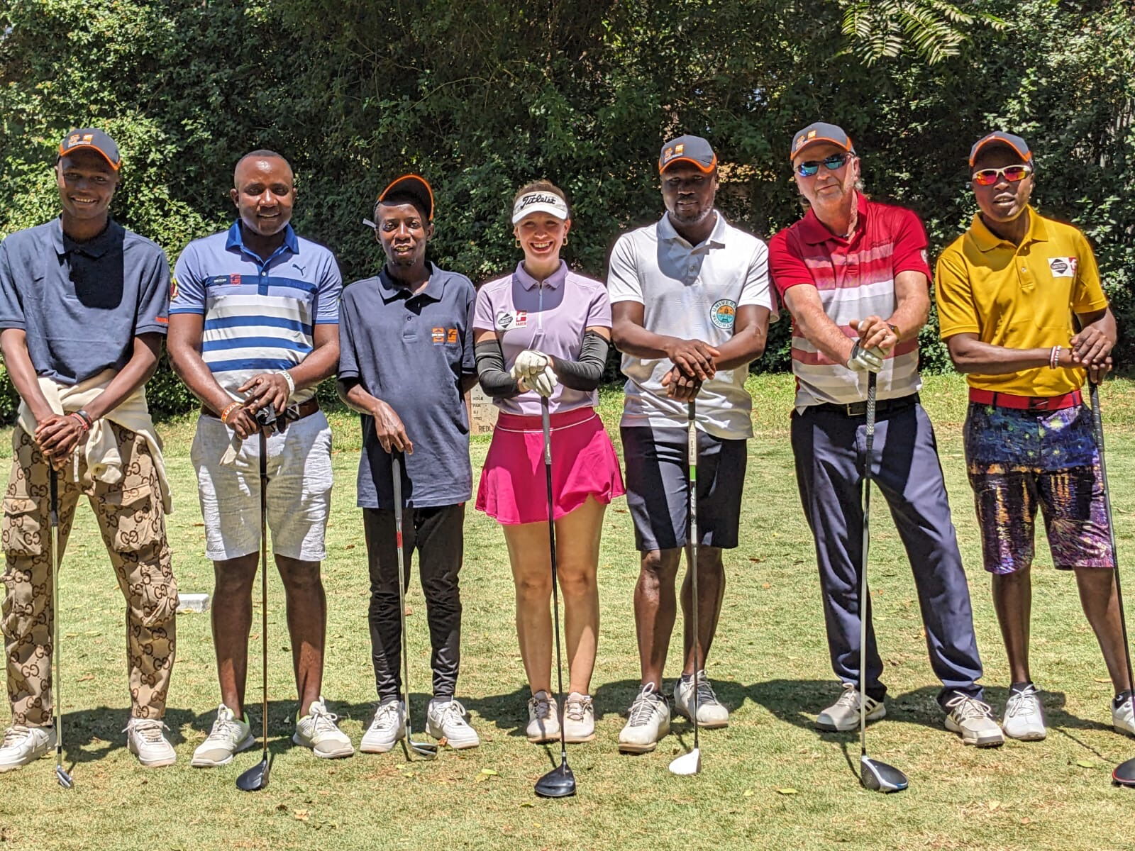 Sieben Golfer stehen mit Schlägern auf einem Golfplatz und posieren für ein Gruppenfoto.
