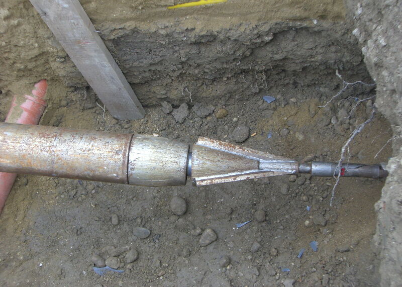 Nahaufnahme eines beschädigten Metallrohrs und einer Kupplung in einem Erdgraben.