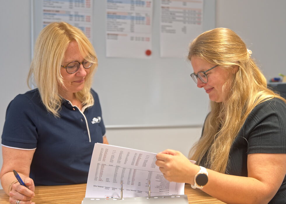 Two women in an office reviewing printed documents together at a table.
