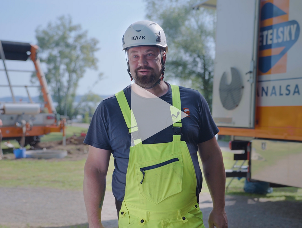 Mann in gelber Warnschutz-Latzhose und Helm steht draußen auf einer Baustelle