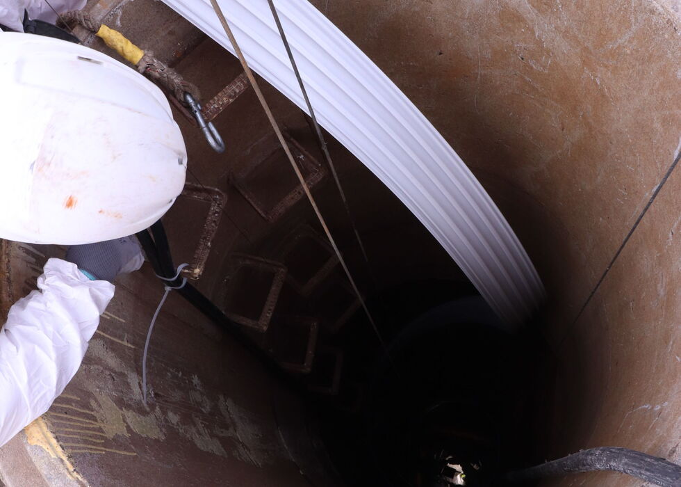 Arbeiter lässt ein weißes Kabel in einen tiefen zylindrischen Schacht hinab zur Inspektion.