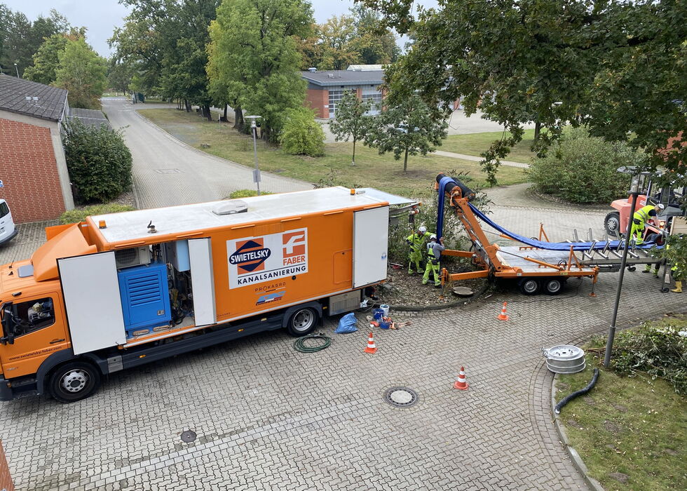 Oranger Versorgungswagen mit Kabelverlegeanhänger und Arbeitern an einer Wohnstraße.