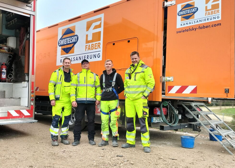 Vier Arbeiter in Warnkleidung stehen vor einem orangefarbenen Faber-Sanierungswagen.