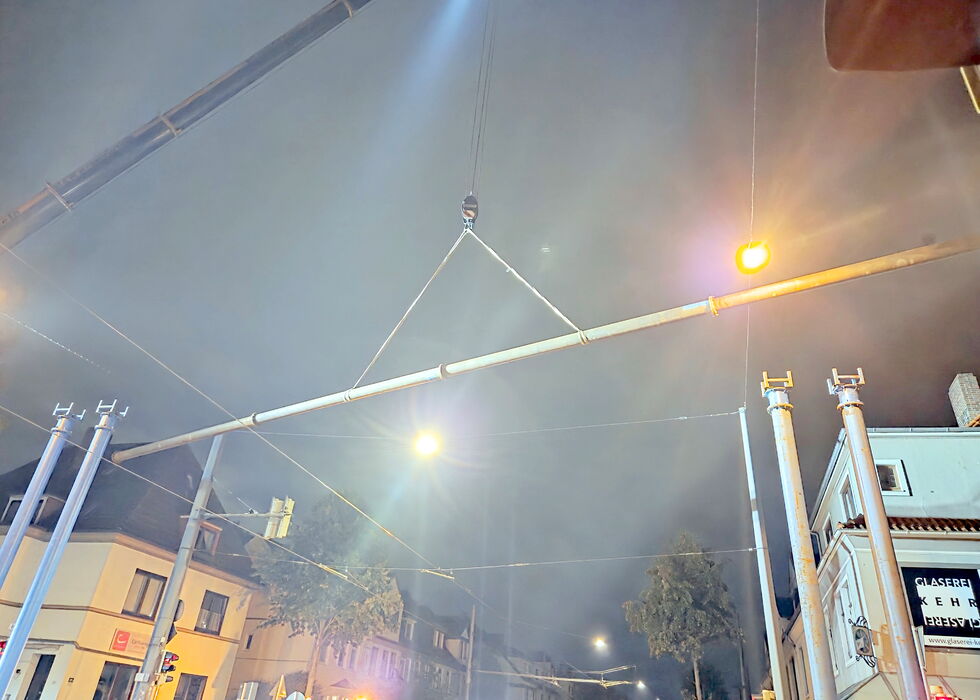 Ein Kran hebt nachts die Bypassleitung über die Stadtstraße, darunter Gebäude und Straßenlaternen.