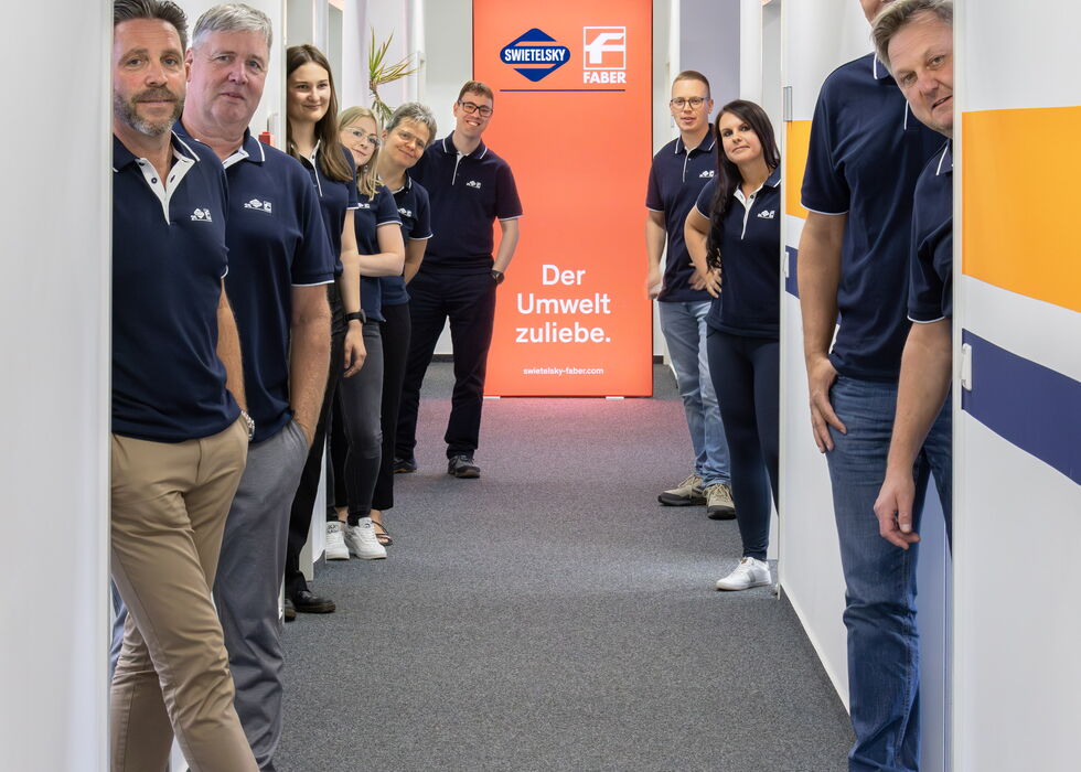 Eine Gruppe von Mitarbeitern steht in einem Bürogang und blickt zur Kamera.