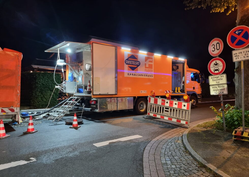 Oranger Straßenreparaturwagen mit Ausrüstung und Pylonen auf einer Straße bei Nacht.