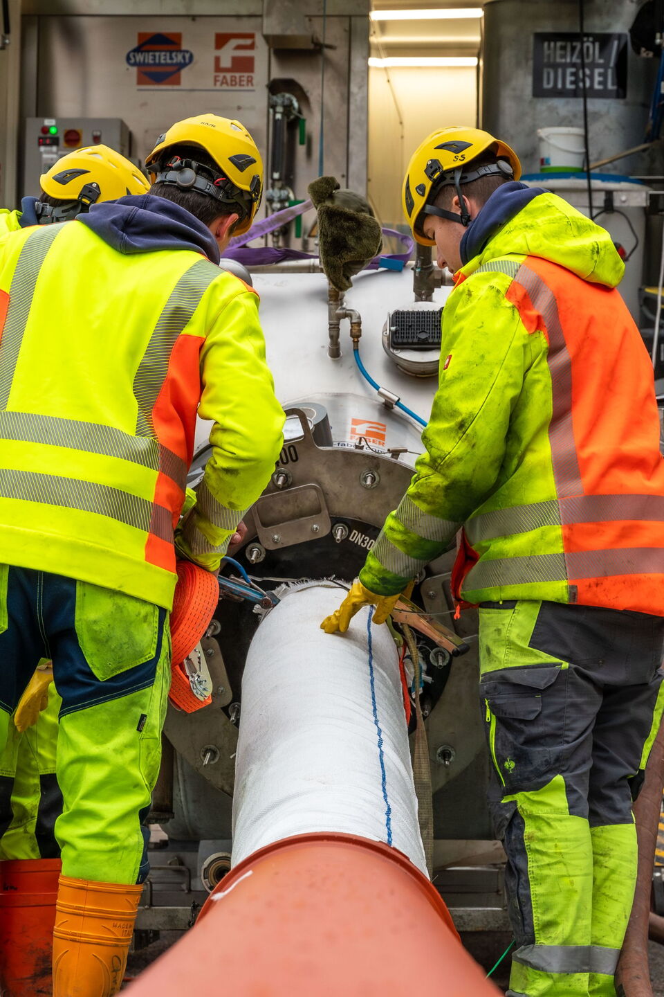 Arbeiter in Warnkleidung überprüfen und handhaben eine große Versorgungsleitung an einer Straßenbaustelle.