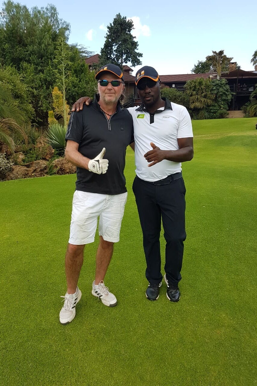 Zwei Männer stehen gemeinsam auf einem Golfplatz und posieren lächelnd auf dem gepflegten Grün.