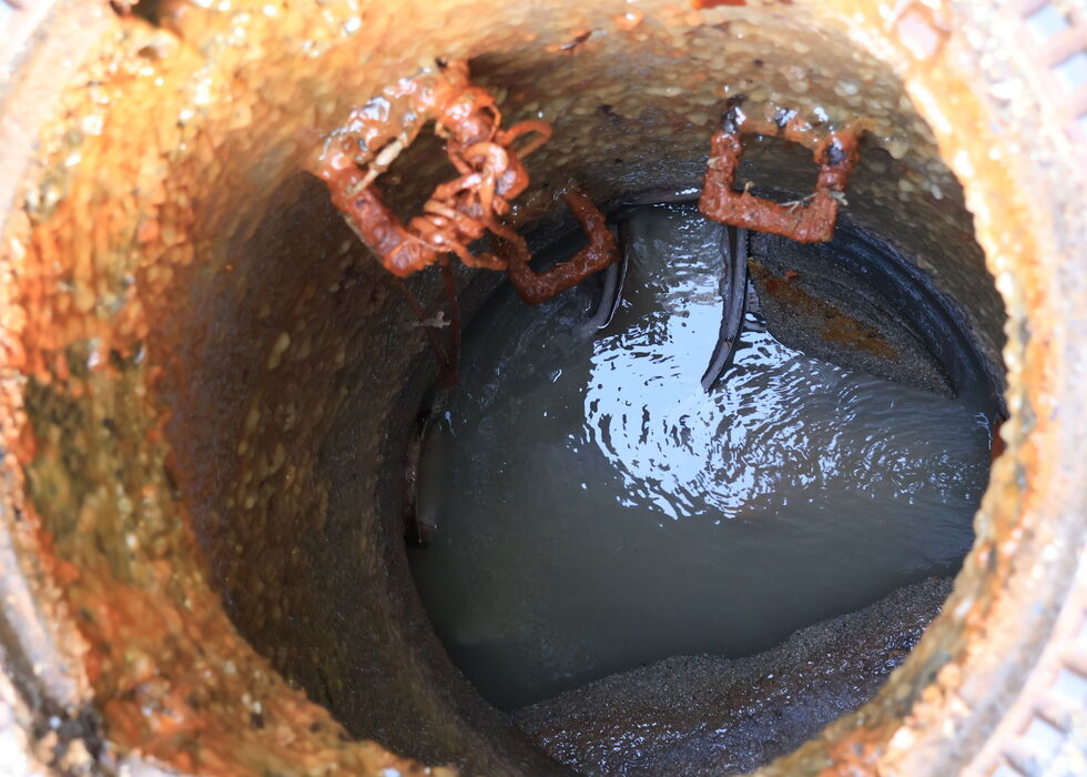Nahaufnahme der Innenseite eines beschädigten Abwasserschachts mit stehendem Wasser, Schmutz und Ablagerungen.