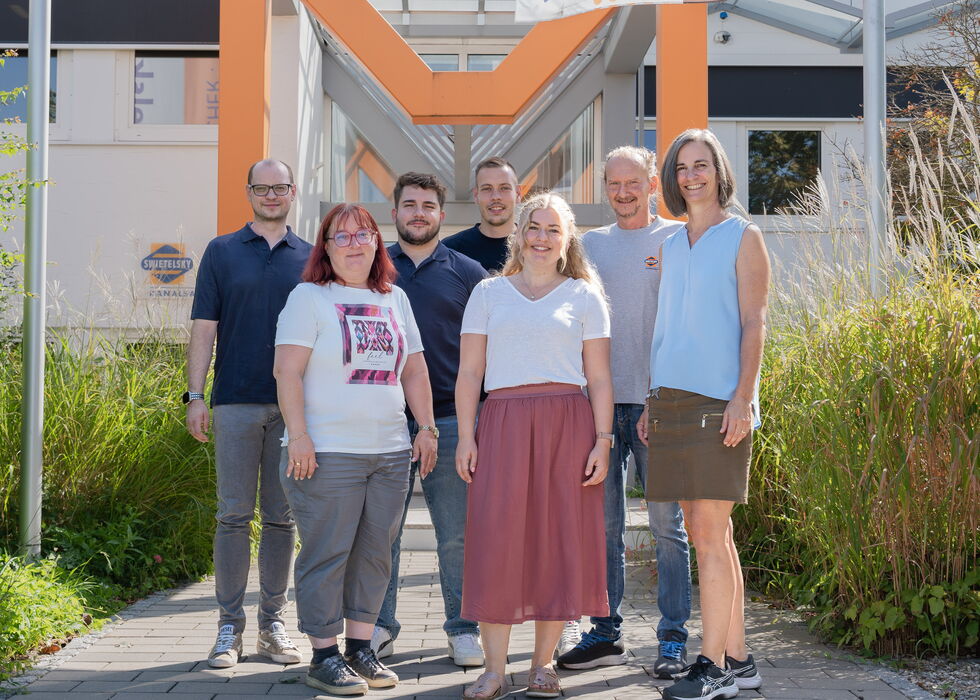 Sechs Kolleginnen und Kollegen stehen gemeinsam im Freien vor einem Bürogebäude.