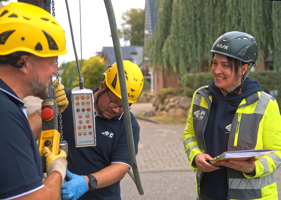 Three rescue workers in helmets and high-visibility gear discuss equipment outdoors.