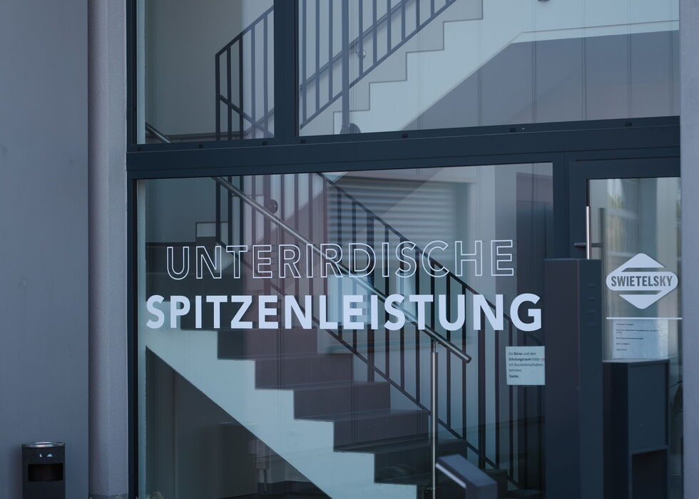Innenansicht eines Treppenhauses mit Geländer und Glasbeschriftung: „Unterstützende Spitzenleistung“.