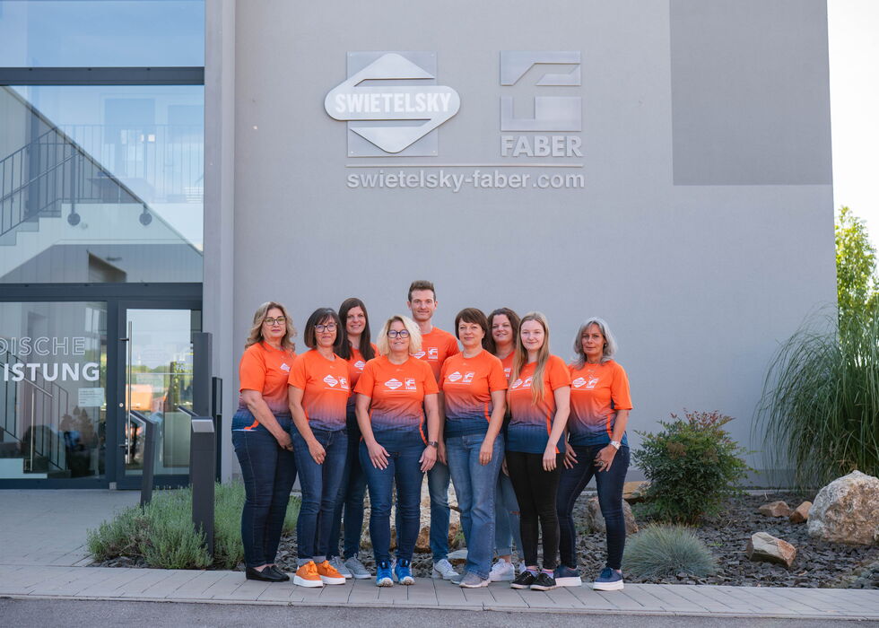Eine Gruppe von Mitarbeitenden in orangefarbenen Shirts vor dem Swietelsky-Faber-Gebäude