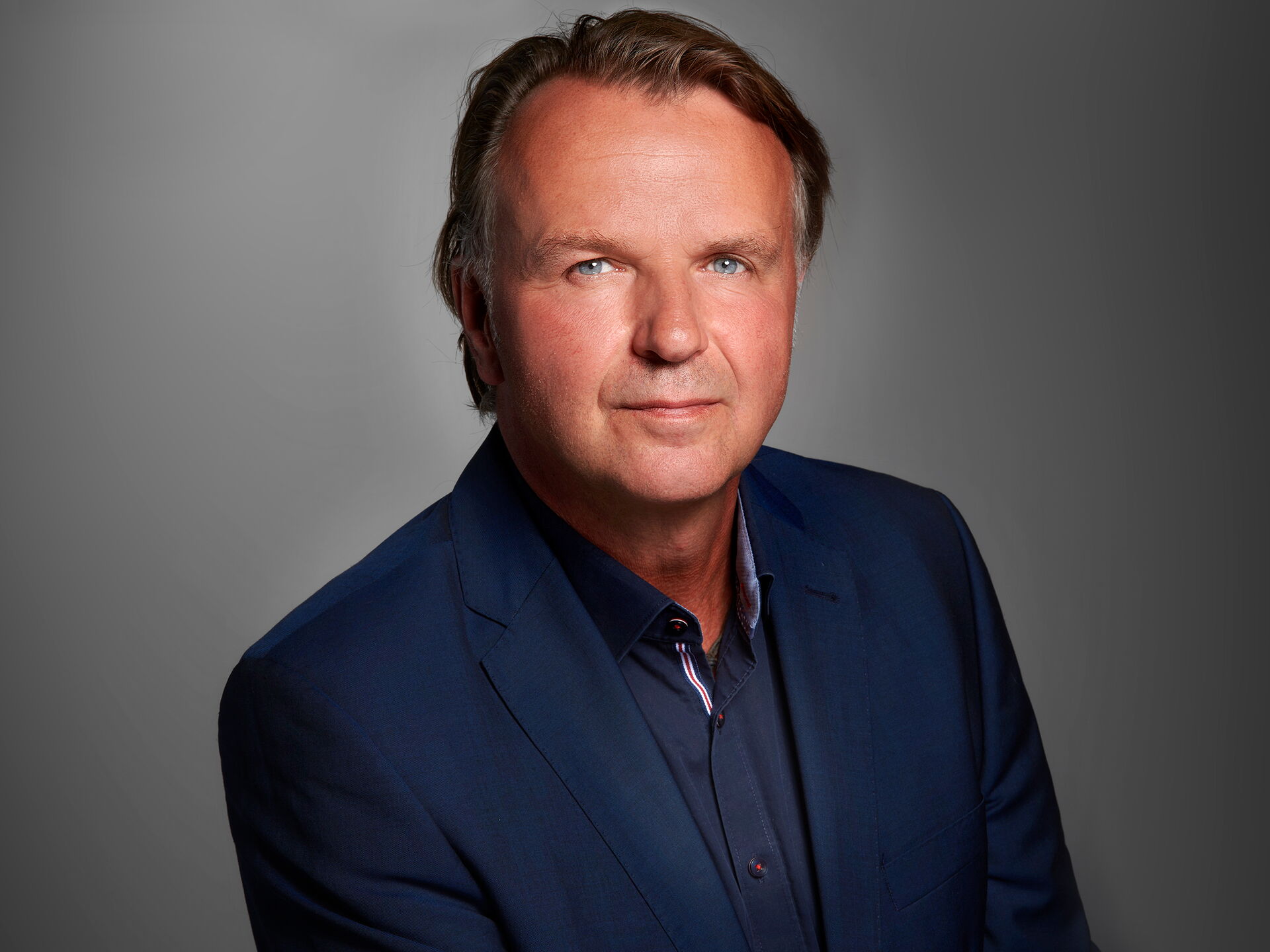 Studio-Porträt Dipl.-Ing. Jörg Brunecker im marineblauen Sakko vor grauem Hintergrund.