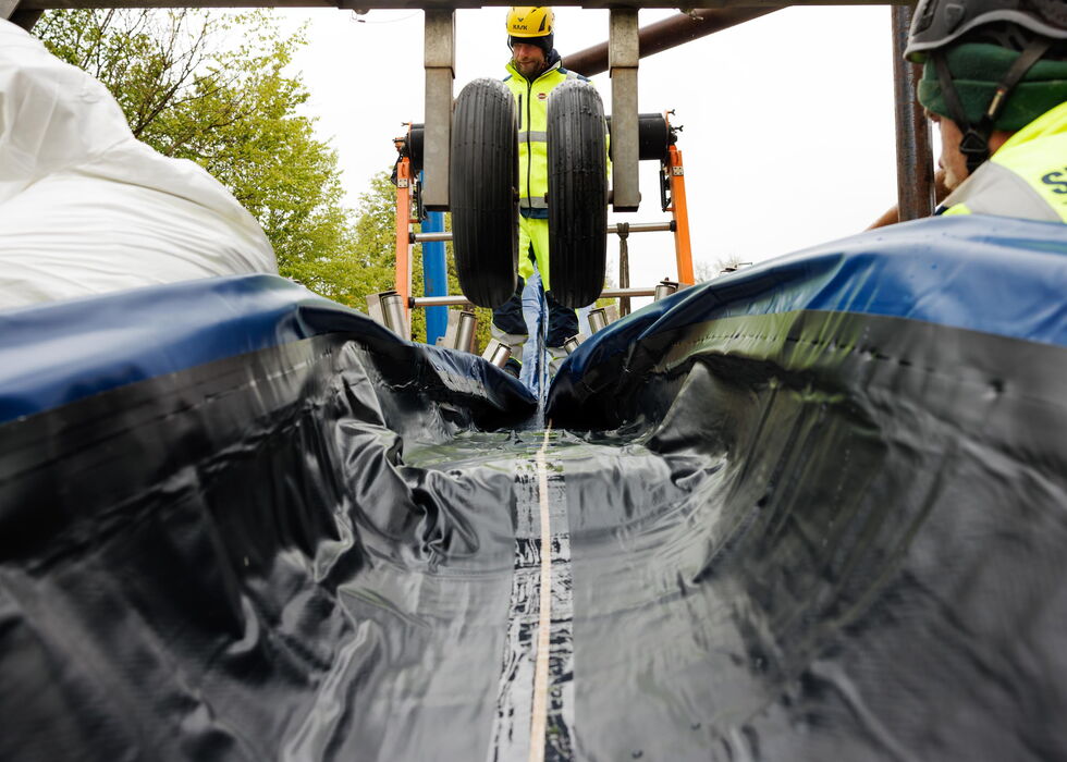 Arbeiter mit Schutzausrüstung stehen an einem wasserdicht ausgekleideten Graben auf einer Baustelle.