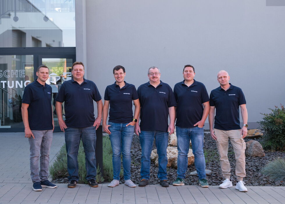 Eine Gruppe von sieben Männern posiert für ein Teamfoto vor einem modernen Gebäude.