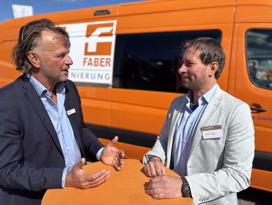 Jörg Brunecker und B_I umweltbau-Chefredakteur Boris Valdix in Businesskleidung sprechen vor einem orangefarbenen Transporter mit Logo der Swietelsky-Faber GmbH