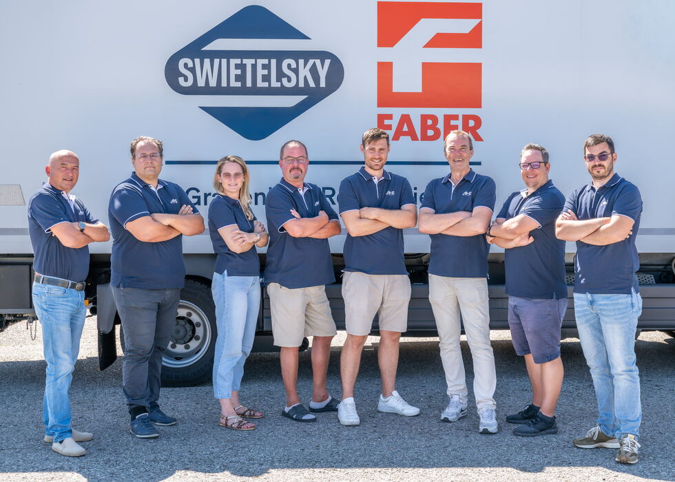Acht Mitarbeitende stehen mit verschränkten Armen vor einem Lkw mit den Logos von Swietelsky und Faber.