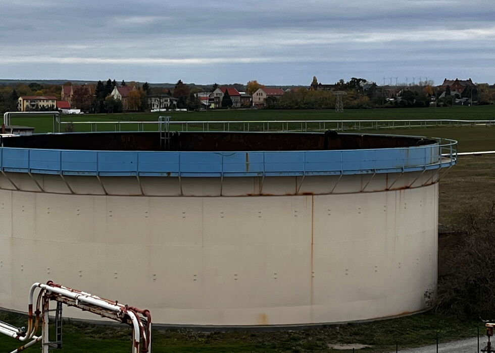 Großer zylindrischer Lagertank in einer Industrieanlage unter bewölktem Himmel.