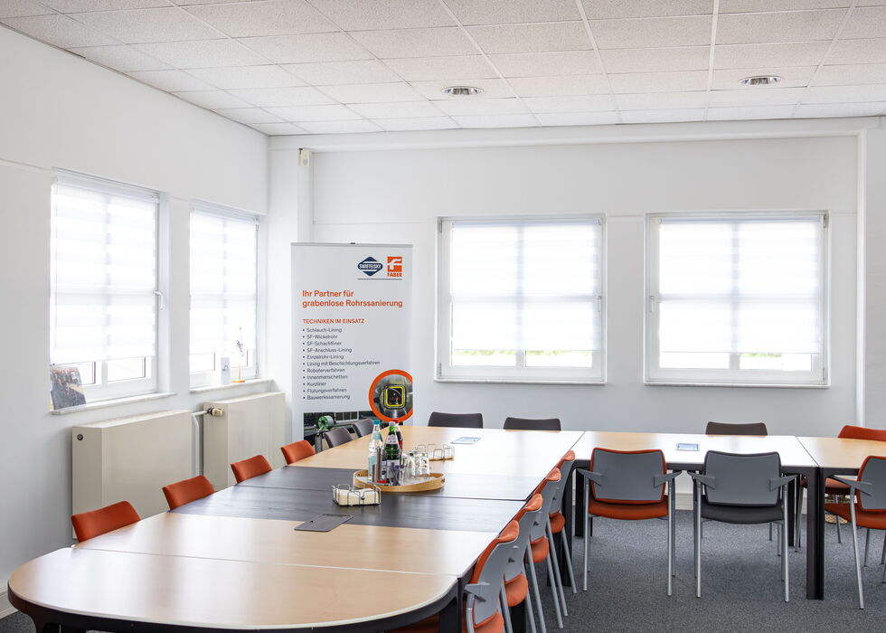 Heller Besprechungsraum mit großem Konferenztisch, Stühlen, Fenstern und einem Banner.