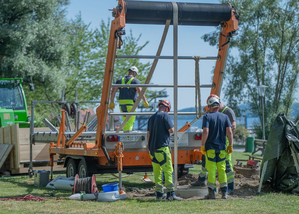 Zwei Bauarbeiter in Schutzkleidung arbeiten im Außenbereich an einem Kranhubrahmen auf einer Wiese.