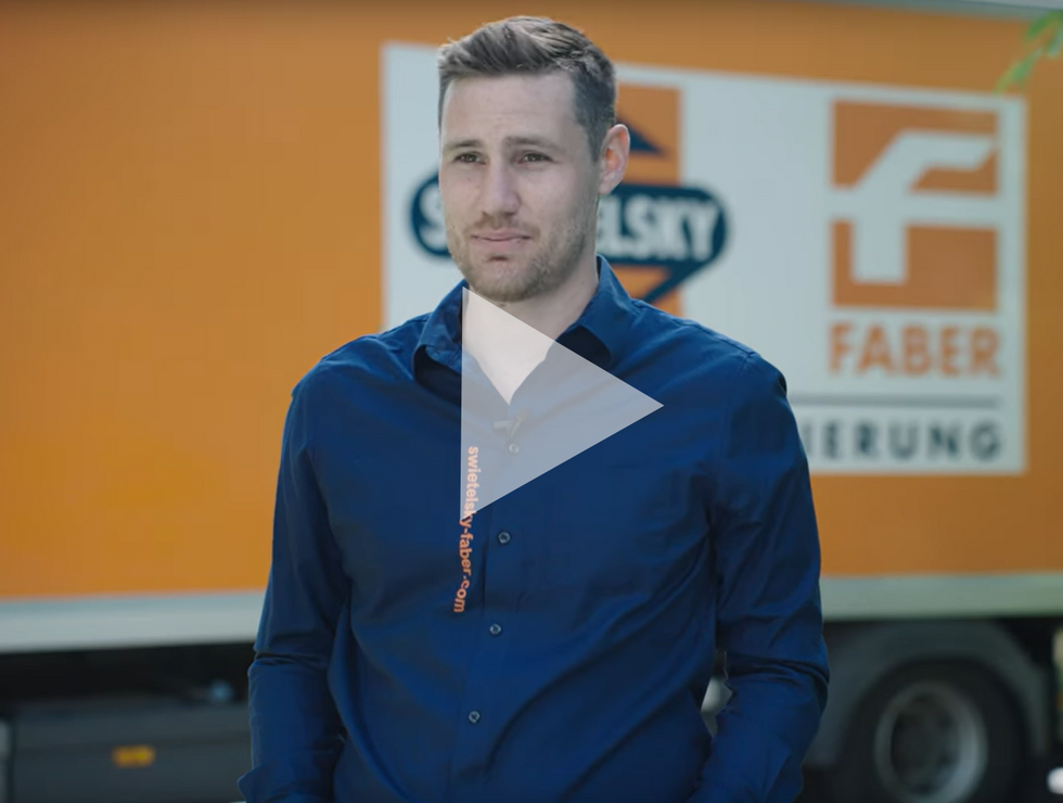 Mann mit kurzen Haaren in dunkelblauem Hemd steht draußen vor einem orangefarbenen Lieferwagen mit Firmenlogos