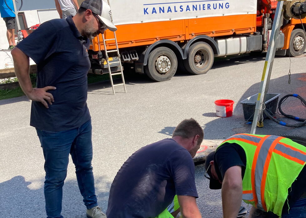 Drei Arbeiter schneiden und reparieren eine beschädigte Straßenoberfläche neben einem Versorgungsfahrzeug.