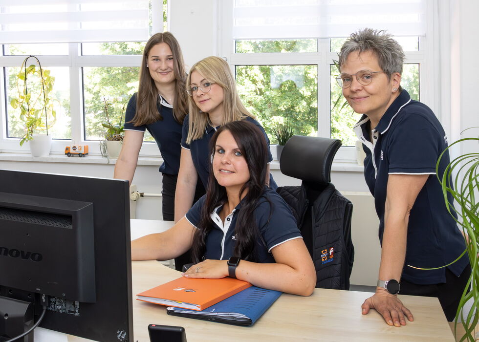 Vier Büroangestellte stehen gemeinsam an einem Computer in einem hellen Arbeitsraum.