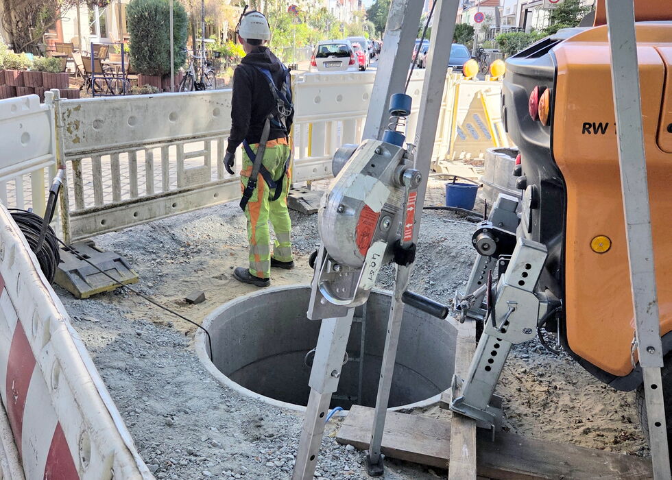 Bauarbeiter an der Straßenbaustelle neben einem offenen Schacht.