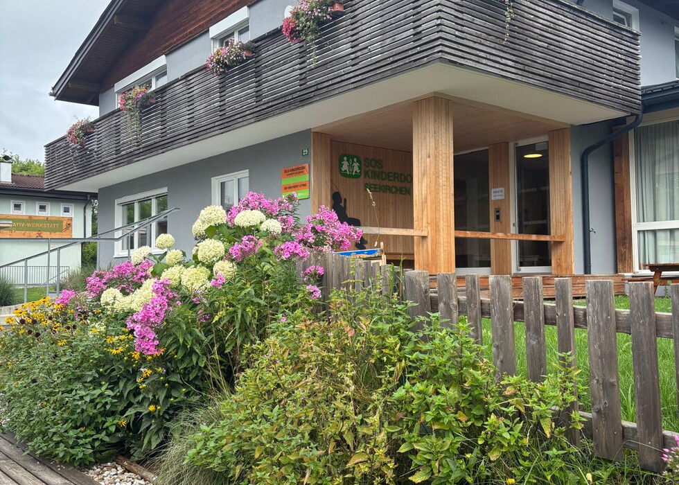 Ein modernes Haus mit Holzbalkon und einem farbenfrohen blühenden Garten davor.