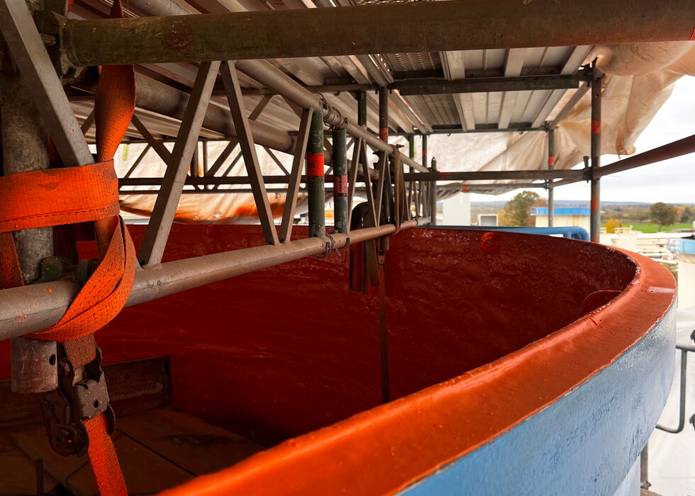 Großer blauer und orangefarbener Industrietank unter Metallgerüst und Trägern.