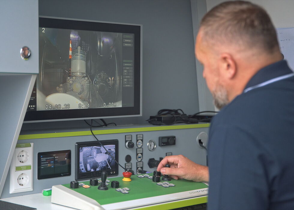 A man operates a control panel while watching a monitor displaying industrial machinery.