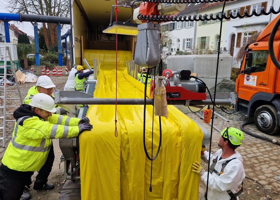 Bauarbeiter in Warnschutzkleidung justieren und sichern Industrieausrüstung neben Fahrzeugen im Außenbereich.