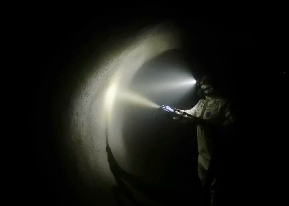 Ein Feuerwehrmann in Schutzkleidung leuchtet mit einer Taschenlampe in einen dunklen Tunnel.