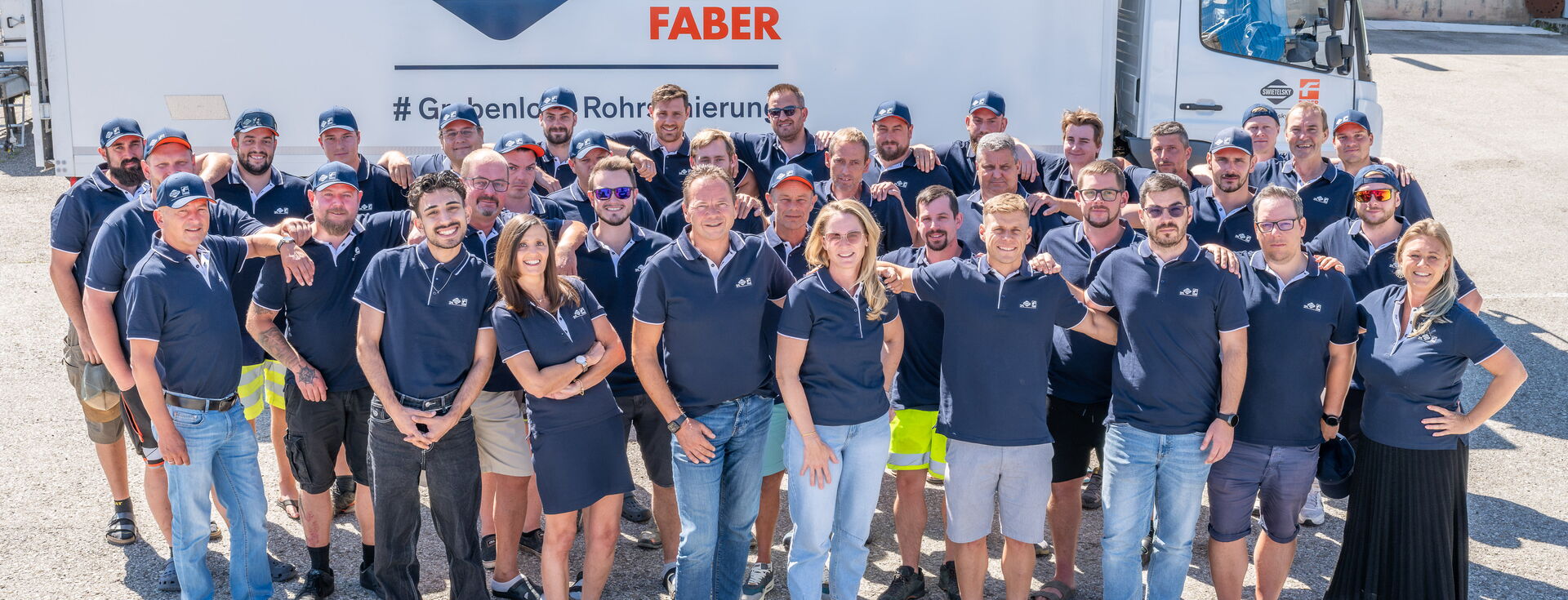 Große Gruppe von Mitarbeitenden posiert gemeinsam vor einem beschrifteten Lkw an einem sonnigen Tag.