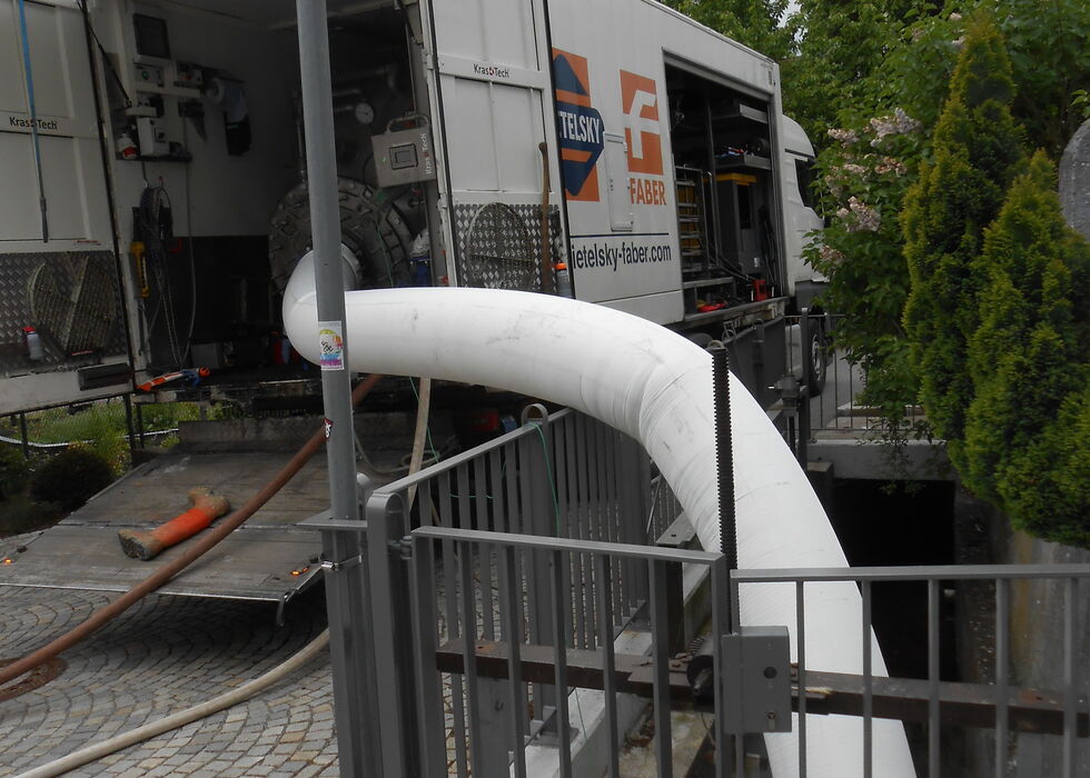 Ein großer weißer Schlauch führt von einem Lkw in einen Graben neben einem gesperrten Gehweg.