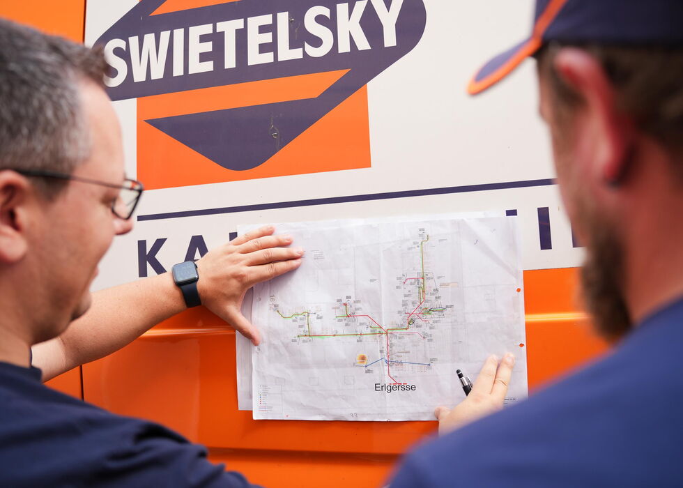 Zwei Mitarbeiter betrachten eine Papierkarte an der Seite eines SWIETELSKY-Fahrzeugs.