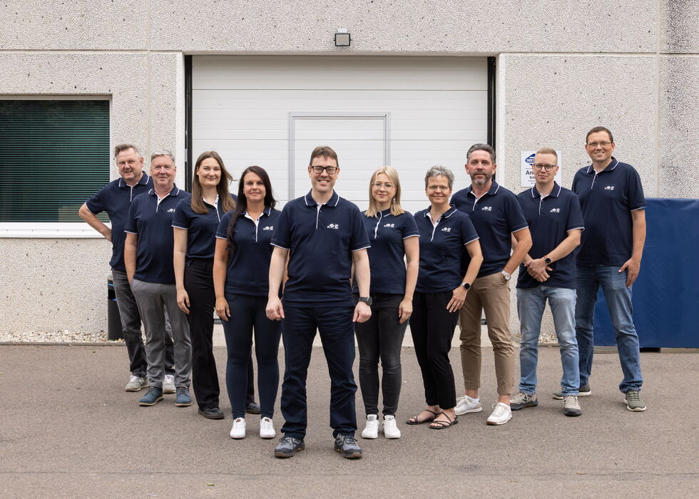 Eine Gruppe von zehn Personen in passenden dunkelblauen Shirts steht zusammen vor einem Gebäude.