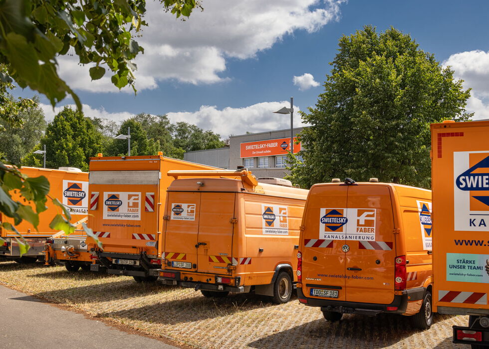 Reihe orangefarbener Servicewagen und Lkw, die an einem sonnigen Tag neben Bäumen stehen.