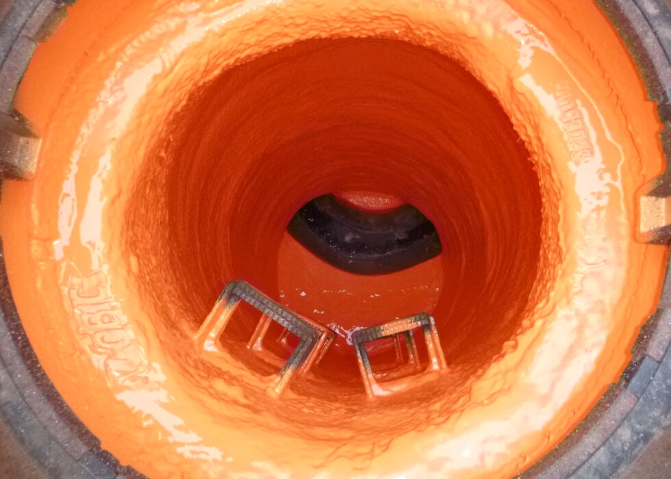 Blick in ein orangefarbenes Industrie-rohr mit Metallbauteilen und einer dunklen Öffnung im Hintergrund.