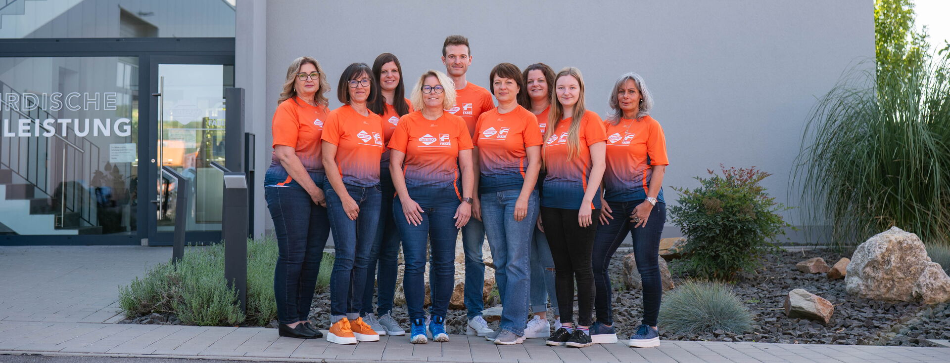 Eine Gruppe von Mitarbeitenden in orangefarbenen Shirts vor dem Swietelsky-Faber-Gebäude
