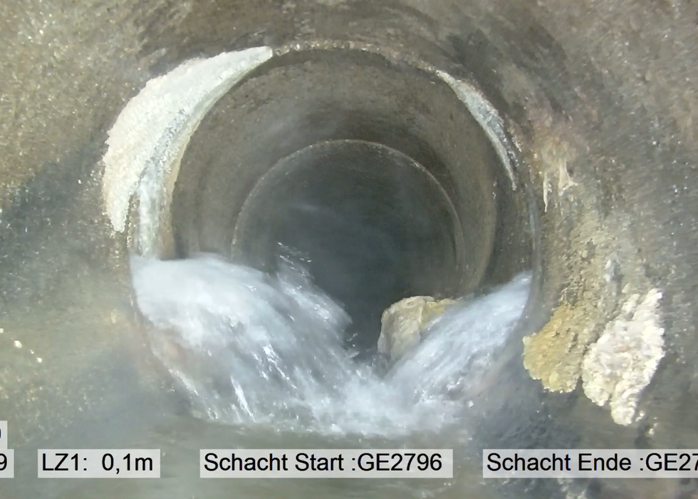 Wasser strömt durch einen runden Betontunnel mit einem kleinen Stein in der Mitte.