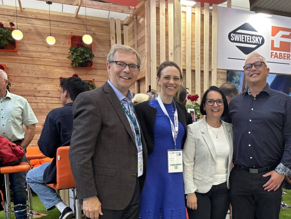 Four people smiling and posing together at an exhibition booth during a trade show.