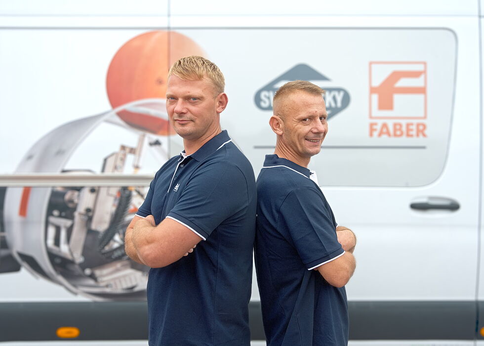 Two men in navy shirts stand back to back in front of a white van with company logos.