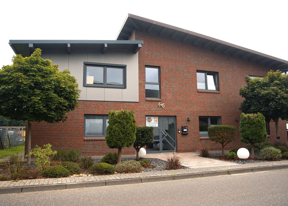 Front view of a modern two-story brick office building with windows, trees, and a small landscaped entrance.