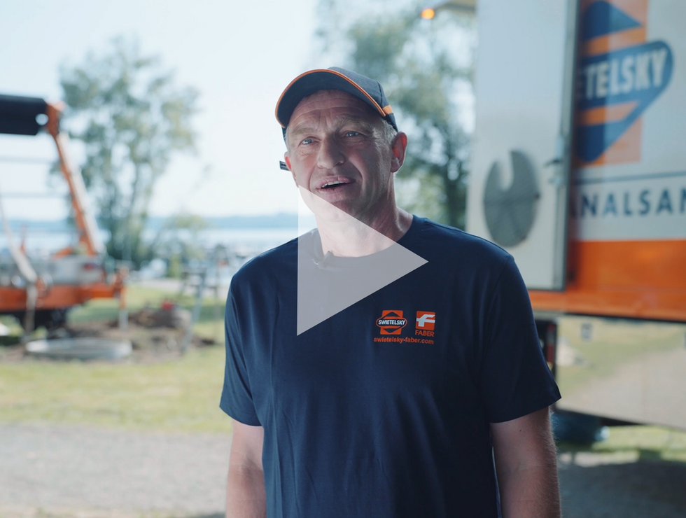 Mann in blauem T-Shirt und Kappe steht im Freien vor Industrieausrüstung und großem orangenen Fahrzeug