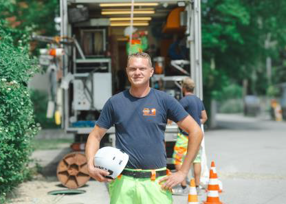 Ein Mann in dunklem T-Shirt und neongrüner Arbeitshose steht neben einem Servicefahrzeug mit Pylonen und Ausrüstung im Hintergrund.