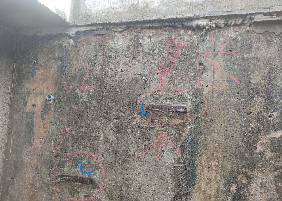 Verwitterte Betonwand mit roten und blauen Markierungen und Ausbesserungsstellen.