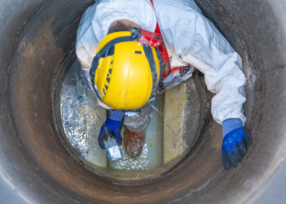 Draufsicht auf einen Arbeiter in Schutzkleidung, der mit einem technischen Geräte das Innere eines Abwasserrohrs untersucht.