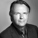 A black and white professional portrait of a man in a suit, showing a confident expression.